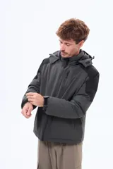 Campera técnica con capucha desmontable, diseño bicolor en negro y gris. Cuenta con cierre frontal termosellado, bolsillos laterales y bolsillo en el pecho con cierre, ideal para protección contra el viento y el frío.