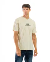 Remera de algodón color beige, de corte clásico con escote en V y manga corta, con estampa frontal centrada con el texto "Lazy Los Angeles" y logotipo superior.