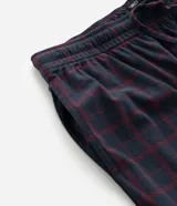 Pantalón de pijama tipo jogger para hombre, confeccionado en tejido plush suave y abrigado. Presenta un diseño estampado a cuadros, cintura elástica con cordón de ajuste y puños elásticos en los tobillos.