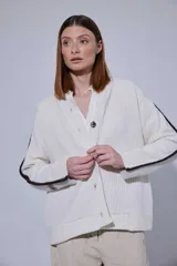 Saco de punto acanalado en color gris claro, con cierre frontal de botones oscuros. Presenta un diseño de bloques de color en las mangas, combinando negro y marrón, y un cuello redondo.