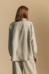 Camisa de manga larga color blanco hueso con finas rayas verticales en color oscuro. Presenta cuello camisero, botones frontales y dos bolsillos superpuestos en el pecho.