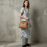 Cartera estilo maletín de cuero sintético en color suela, con manija superior y correa ajustable y desmontable para usar al hombro o cruzada. Cuenta con cierre de solapa metálica y estructura rígida.