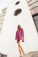 Vestido corto de tejido calado a rayas verticales en tonos blanco, lila, amarillo y borgoña, con mangas largas y terminaciones con puntilla.