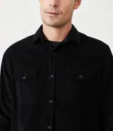 Camisa de hombre color verde oscuro, confeccionada en terciopelo, con cuello clásico, manga larga y dos bolsillos frontales con solapa y botón. Cierre frontal con botones.