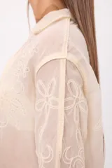 Camisa de encaje color crema con diseño floral bordado, cuello camisero, cierre frontal con botones y mangas largas con terminación acampanada.