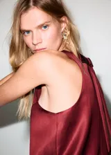 Vestido corto de tejido satinado en color bordó, sin mangas, con cuello redondo y diseño recto.