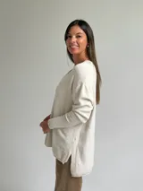Sweater de punto color beige con escote en V, diseño holgado y costura central vertical. Presenta mangas largas con puños acanalados y ruedo con terminación acanalada.