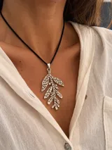 Collar tipo tiento de cuero gamuzado negro con dije colgante de acero en forma de rama con hojas texturizadas.