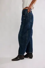 Jean de denim azul con silueta barrel y tiro medio, piernas amplias que se afinan en los tobillos, desgastes sutiles y costuras en las piernas.