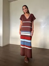 Vestido largo de tejido de punto de algodón, con diseño rayado en tonos marrón, celeste, blanco y rojo. Presenta escote en V con detalle de costura en contraste, mangas cortas, silueta holgada y aberturas laterales en el dobladillo.