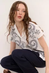 Camisa blanca de manga corta con cuello solapa, cierre frontal de botones y diseño bordado en hilo azul marino con motivos florales y vegetales.
