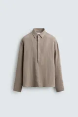 Camisa de corte regular confeccionada en lino, con cuello solapa y cierre frontal de botonadura oculta. Presenta mangas largas con puños abotonados.