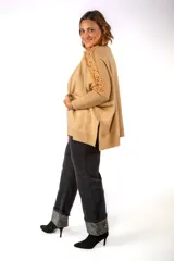 Sweater de punto color beige, con cuello alto y diseño holgado. Presenta detalles de encaje floral en los hombros y mangas, con puños acanalados.