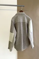 Camisa estilo leñadora con diseño patchwork en tonos marrones y beige. Presenta coderas, cartera americana y bolsillo ojal en el delantero. Confeccionada en Uruguay con tela 100% lana fina sin teñir.