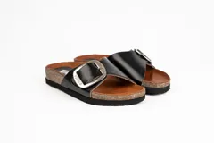 Sandalia de cuero negra con plantilla marrón y base de corcho. Presenta una tira ancha sobre el empeine con hebilla metálica plateada.