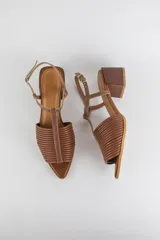 Sandalias de cuero color marrón, con diseño de punta fina, tiras tubulares fruncidas en el empeine, tira vertical tipo T y taco cuadrado de altura media. Cuentan con tira ajustable al tobillo con hebilla metálica.