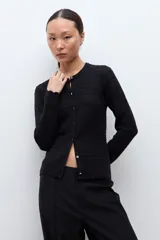 Cardigan negro de manga larga con cuello redondo y cierre frontal de botones. Presenta un tejido con patrones estructurados y un borde festoneado en el dobladillo.