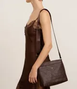 Bandolera femenina confeccionada en material sintético color marrón con efecto embossed, modelo transversal postman con cierre por cremallera, bolsillo externo y asa larga de grosgrain.