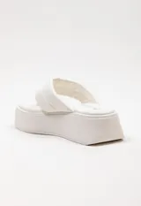 Sandalia tipo ojota con plataforma, confeccionada en material sintético color blanco. Presenta una tira ancha acolchada con detalle de costura central y diseño de separación para el dedo.