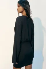 Vestido corto de manga larga confeccionado en punto elástico de color negro, con escote redondo, cuerpo holgado y falda entallada.