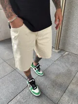 Bermuda de corte baggy en color arena, confeccionada en tejido de algodón resistente, con diseño de cinco bolsillos y cierre frontal con botón y cremallera.