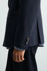 Blazer regular fit color azul marino, confeccionada en tejido con lana. Presenta cuello con solapas de pico, manga larga con puño abotonado, bolsillos de vivo en el pecho y de plastrón en la cadera. Incluye un bolsillo interior y aberturas en la espalda. El cierre es frontal con botonadura cruzada.