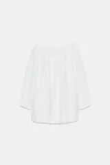 Blusa blanca de lino con escote recto y hombros descubiertos, manga abullonada tres cuartos terminada en elástico.