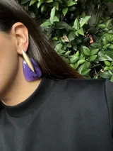 Aros colgantes con base de resina color violeta con detalles en negro y pieza metálica dorada opaca en forma de lanza.
