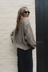 Saco tejido de punto con diseño de ochos y trenzas, color azul marino. Presenta cierre frontal con botones en contraste de color turquesa y un delicado bordado a mano en el pecho.