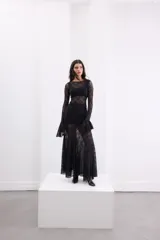 Vestido largo de encaje negro con transparencias, corte ajustado al cuerpo, mangas largas con terminación acampanada y falda con caída fluida.