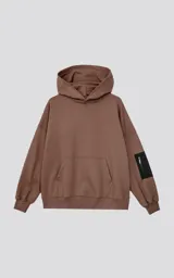 Hoodie oversize color marrón, confeccionado en algodón rústico. Presenta capucha forrada, bolsillo frontal tipo canguro y un bolsillo utilitario con cierre en la manga izquierda, con detalles en microfibra.