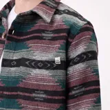 Camisa de franela con diseño de estampado geométrico étnico en tonos verdes, rosas y negros. Presenta cuello clásico, cierre frontal con botones y mangas largas.