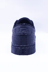 Zapatilla urbana de caña baja, color negro, con cordones negros y suela de goma negra. Presenta microperforaciones en el lateral y un logo de pingüino en relieve en el centro.