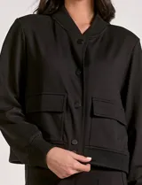 Camperita tipo bomber color beige claro, con cuello redondo acanalado, cierre frontal con broches metálicos y bolsillos delanteros con tapa. Los puños y el bajo son acanalados.