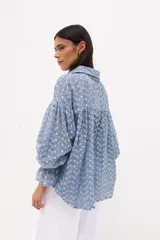 Camisa celeste a rayas verticales blancas, con cuello clásico, cierre frontal con botones y mangas largas abullonadas con puños elásticos.