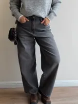 Pantalón de jean estilo mom fit en color gris, con tiro alto y corte holgado de pierna recta. Presenta cierre frontal con botón y bolsillos laterales.