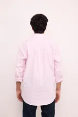 Camisa de corte clásico confeccionada en algodón, con diseño de rayas verticales finas en color rosa sobre fondo blanco. Presenta cuello abotonado, cierre frontal con botones, mangas largas con puños abotonados y un bolsillo en el pecho con el logo de la marca bordado.