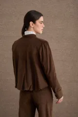 Chaqueta de corte corto y holgado, confeccionada en pana color marrón, con cuello mao, cierre frontal de botones dorados y mangas largas con puños rectos.