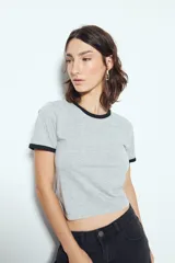 Remera cropped blanca de manga corta, con cuello redondo y terminaciones en contraste de color marrón en cuello y mangas. Inspirada en los clásicos de los años 80.