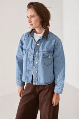 Campera de jean de corte regular estilo camisera, con cuello de pana en color marrón, cierre frontal con botones metálicos dorados y bolsillos frontales con solapa.