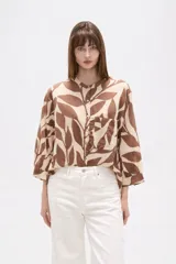 Camisa de corte holgado con estampado botánico en tonos marrones y beige. Presenta cuello mao, cierre frontal con botones y un bolsillo aplicado en el pecho.