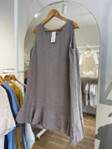 Vestido corto sin mangas, color gris topo, con escote redondo y detalle de volado en el ruedo. El tejido presenta una textura arrugada característica del lino.