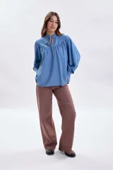 Blusa de jean de corte holgado en color azul claro, con cuello alto fruncido, lazo de ajuste en el escote y mangas largas abullonadas con puños abotonados.