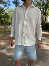 Camisa de lino blanca con rayas verticales beige, de manga larga, cuello camisero y cierre frontal de botones.