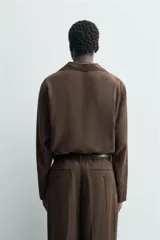 Camisa de manga larga color marrón oscuro, con cuello solapa y abertura frontal, confeccionada en tejido fluido con mezcla de modal. Presenta un calce relajado y aberturas laterales en el bajo.