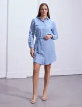 Vestido camisero corto a rayas verticales celestes y blancas, con cuello con solapa, abertura frontal con botones, dos bolsillos de parche en el pecho y lazo de ajuste en la cintura.