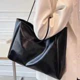 Bolso tipo tote bag color beige claro, de material sintético liso con caída suave. Posee dos asas delgadas para llevar al hombro.