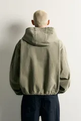 Cazadora de denim de algodón color negro con efecto lavado, de corte relaxed fit, manga larga y capucha. Cuenta con cierre frontal de cremallera, bolsillos frontales tipo canguro y acabados con elástico en puños y cintura.