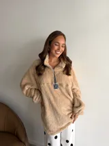 Buzo de corderito color marrón, con cuello alto y cierre frontal parcial. Presenta un diseño holgado con mangas largas y un parche decorativo en el frente.