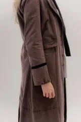 Tapado largo de jean azul oscuro, con cuello solapa y puños con detalle de cinta de terciopelo negro. Presenta costuras visibles que definen paneles y un logo bordado en la espalda.